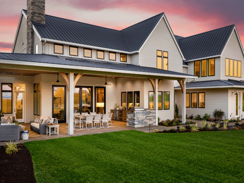 Modern farmhouse with metal roof, large patio, and beautifully landscaped yard at sunset